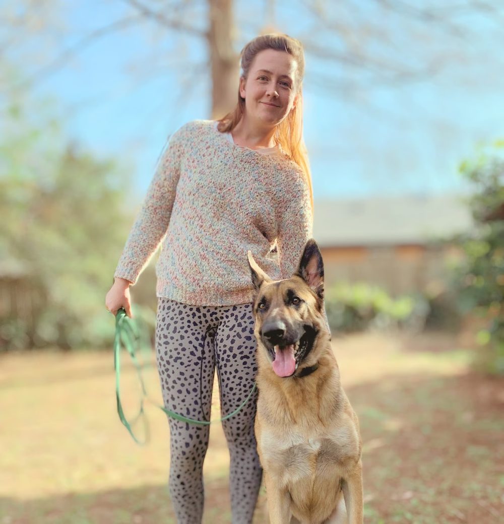 Marta standing outdoors beside a relaxed German shepherd on a long line